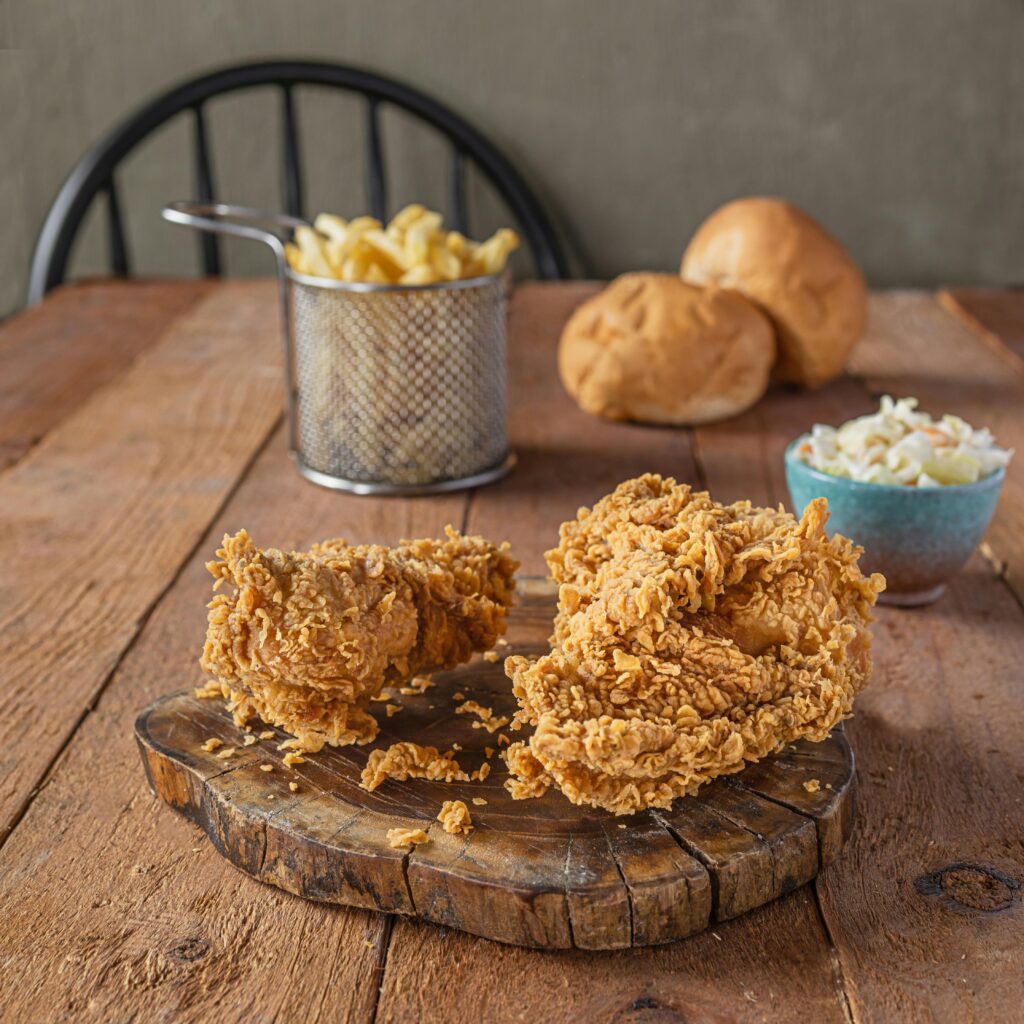Delicious crispy fried chicken served with fries, bread rolls, and coleslaw on a rustic wooden table.